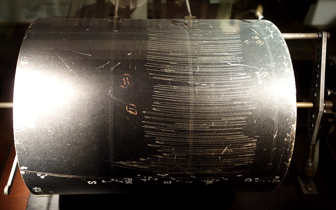 Tambor registrador de un sismógrafo con el papel cubierto de trazos de tinta.